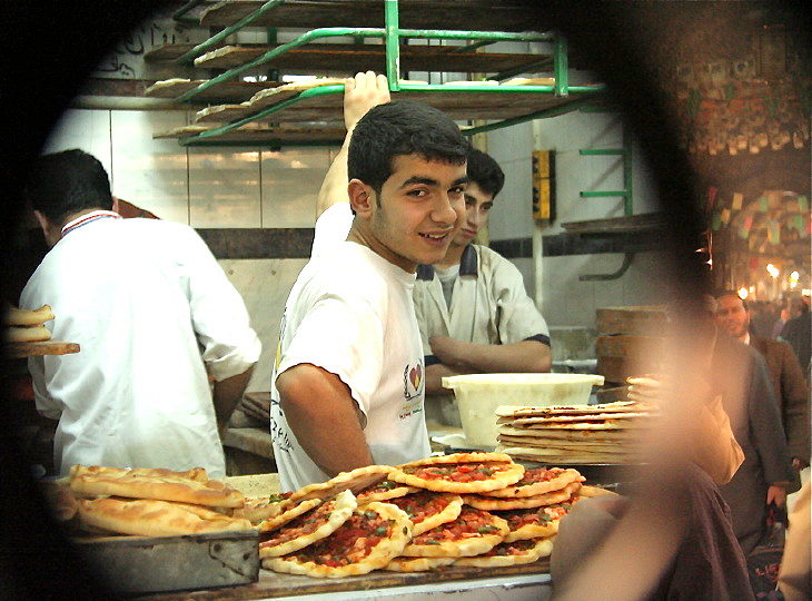 Jungs in einer Bäckerei in der Medina von Aleppo / Syrien: Unbemerkte 90-Grad-Aufnahme ds Hauptmotivs mittels Winkelspiegels. Rechts sind Besucher und Einkaufende zu sehen. 